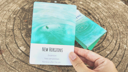 Hand holding a card with 'New Horizons' text on a wooden surface