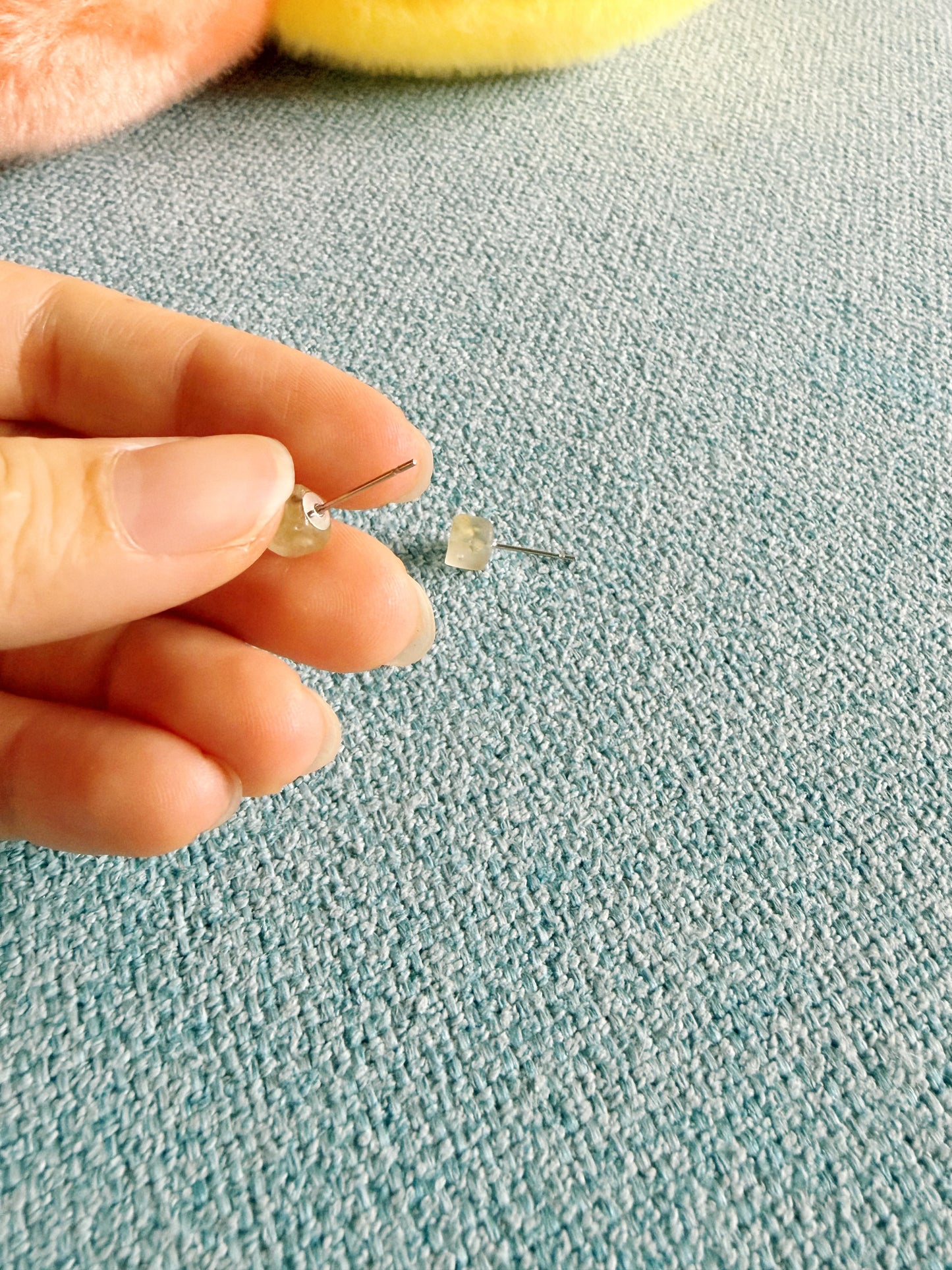 Peridot stud earrings held between fingers highlighting tiny everyday size