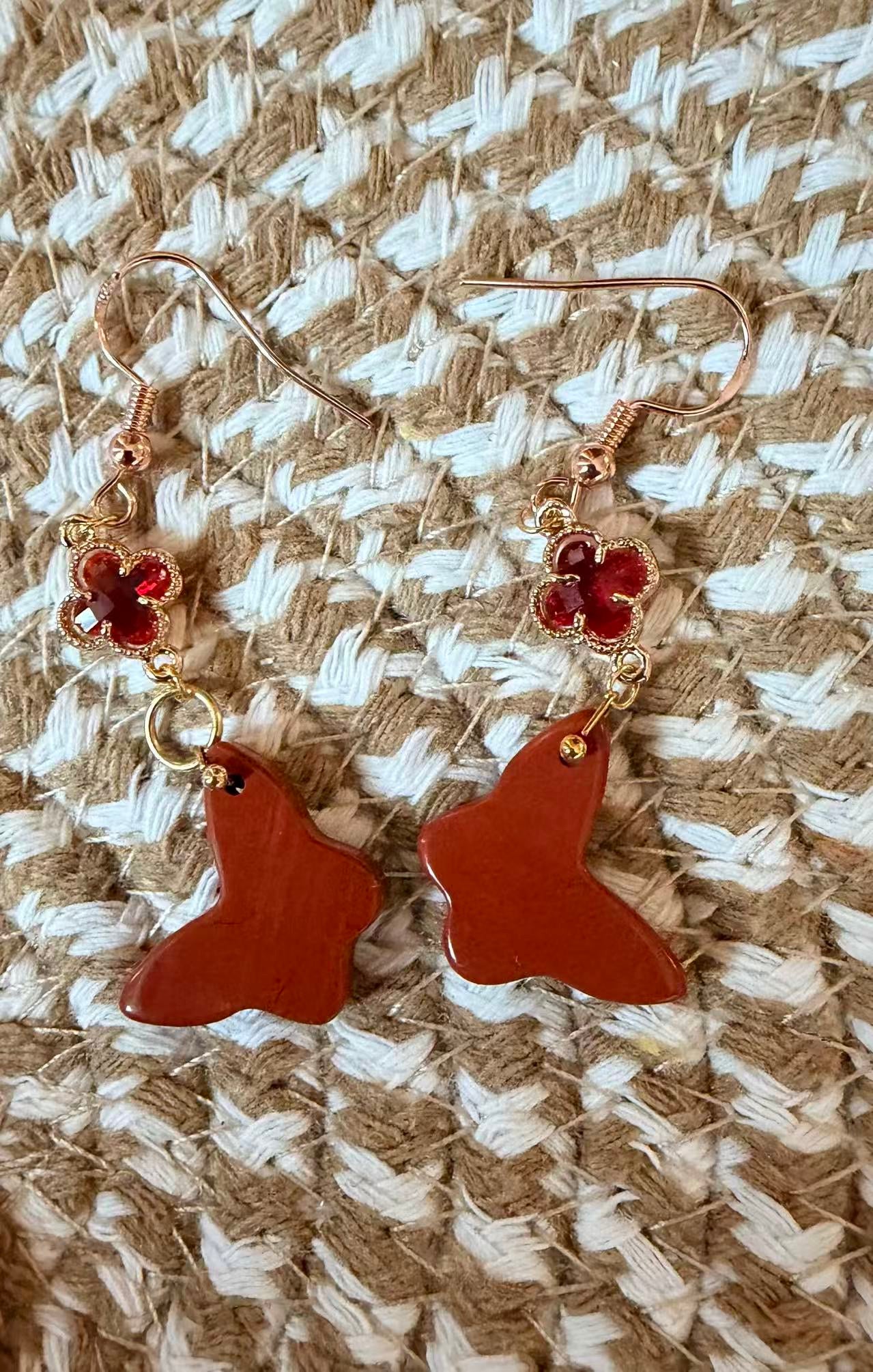 Close-up details of red jasper butterfly earrings with clover detail in gold tone setting