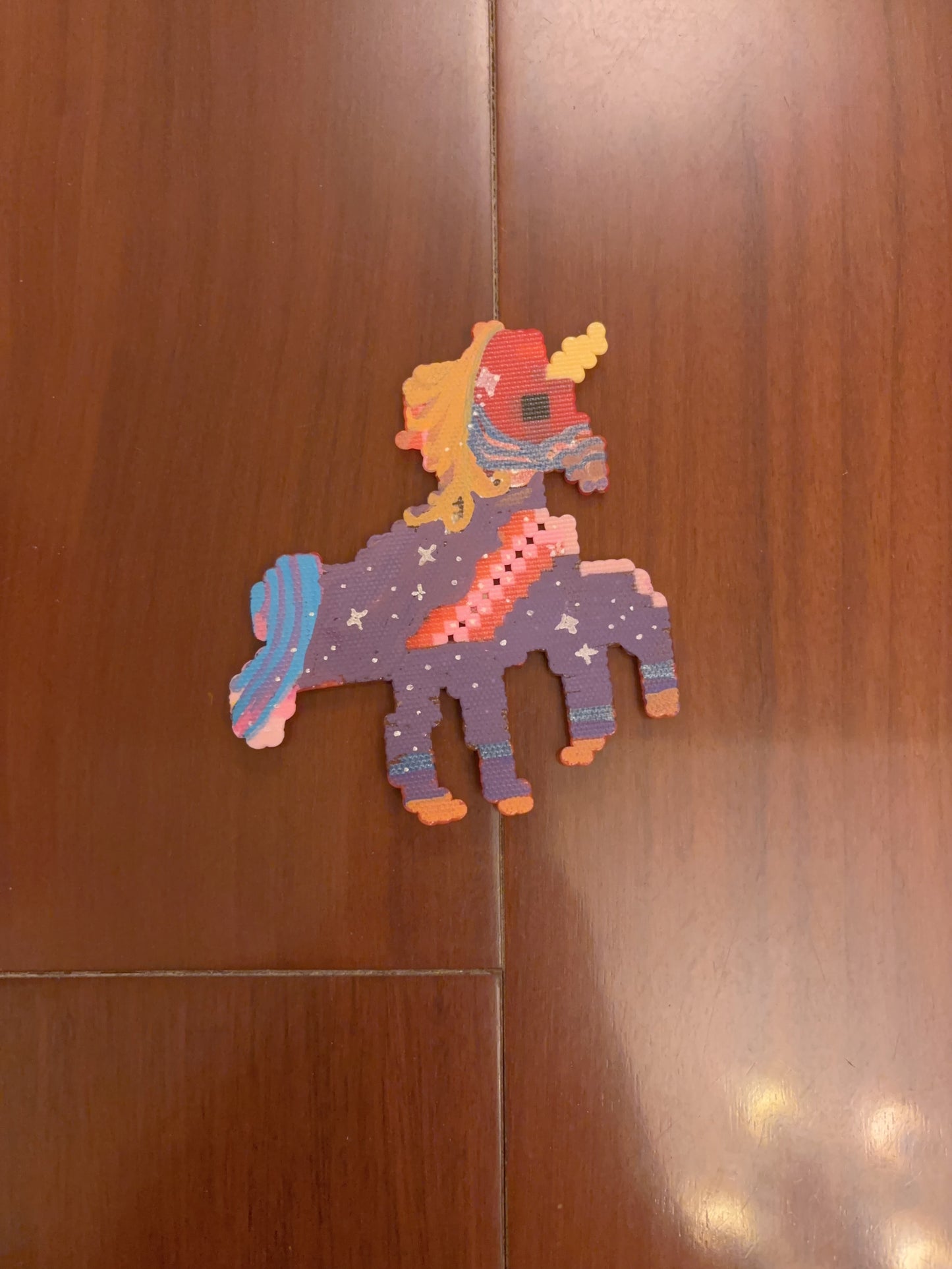 Colorful handmade pixel art unicorn keychain displayed against a wooden background, showcasing a custom bead-by-bead design by Zenlyart Studio.