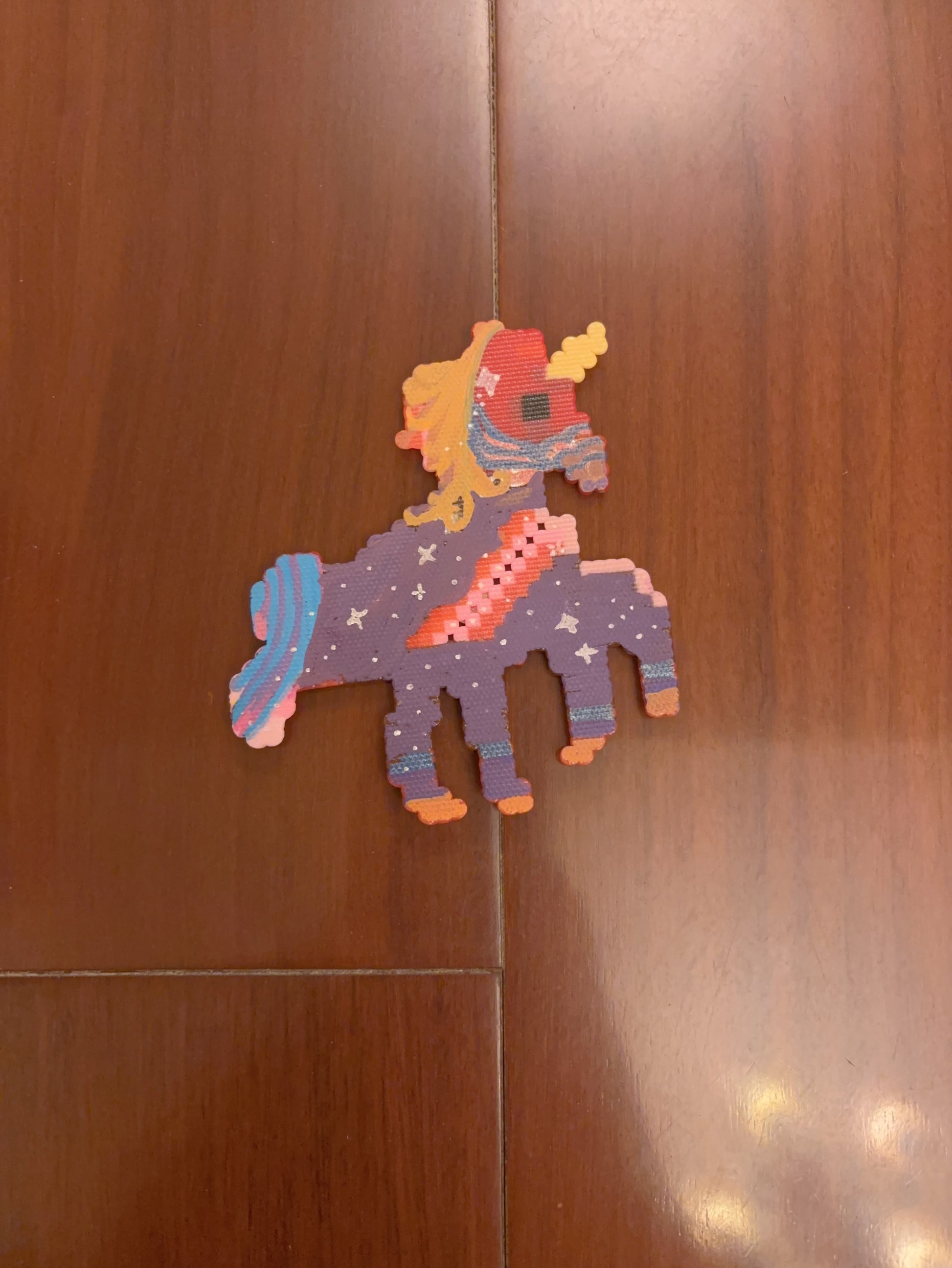 Colorful handmade pixel art unicorn keychain displayed against a wooden background, showcasing a custom bead-by-bead design by Zenlyart Studio.