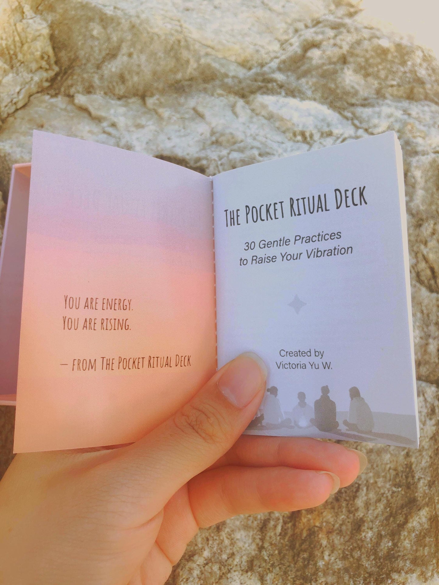 Hand flipping through the first page of 'The Pocket Ritual Deck' against a stone background