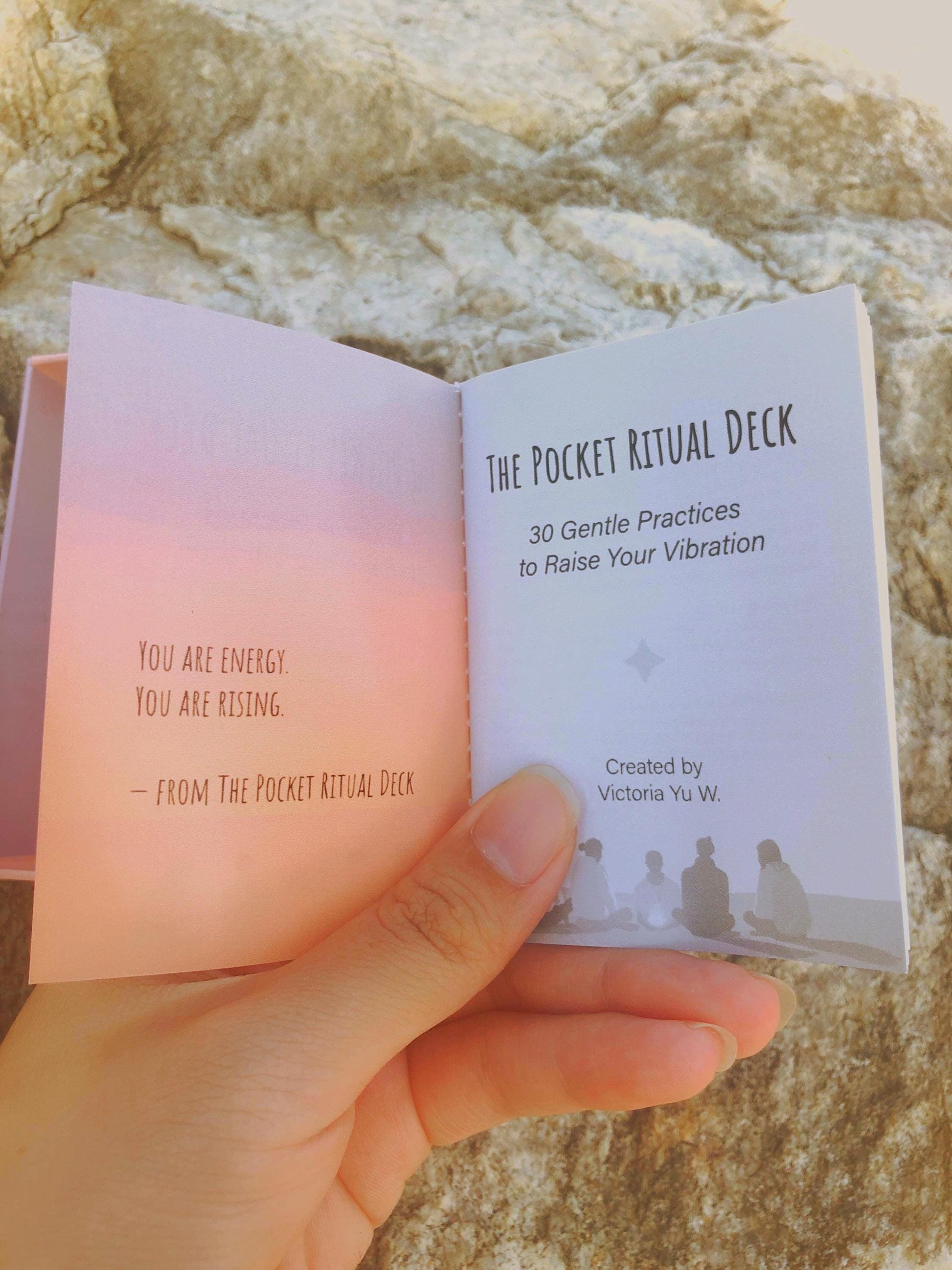Hand flipping through the first page of 'The Pocket Ritual Deck' against a stone background