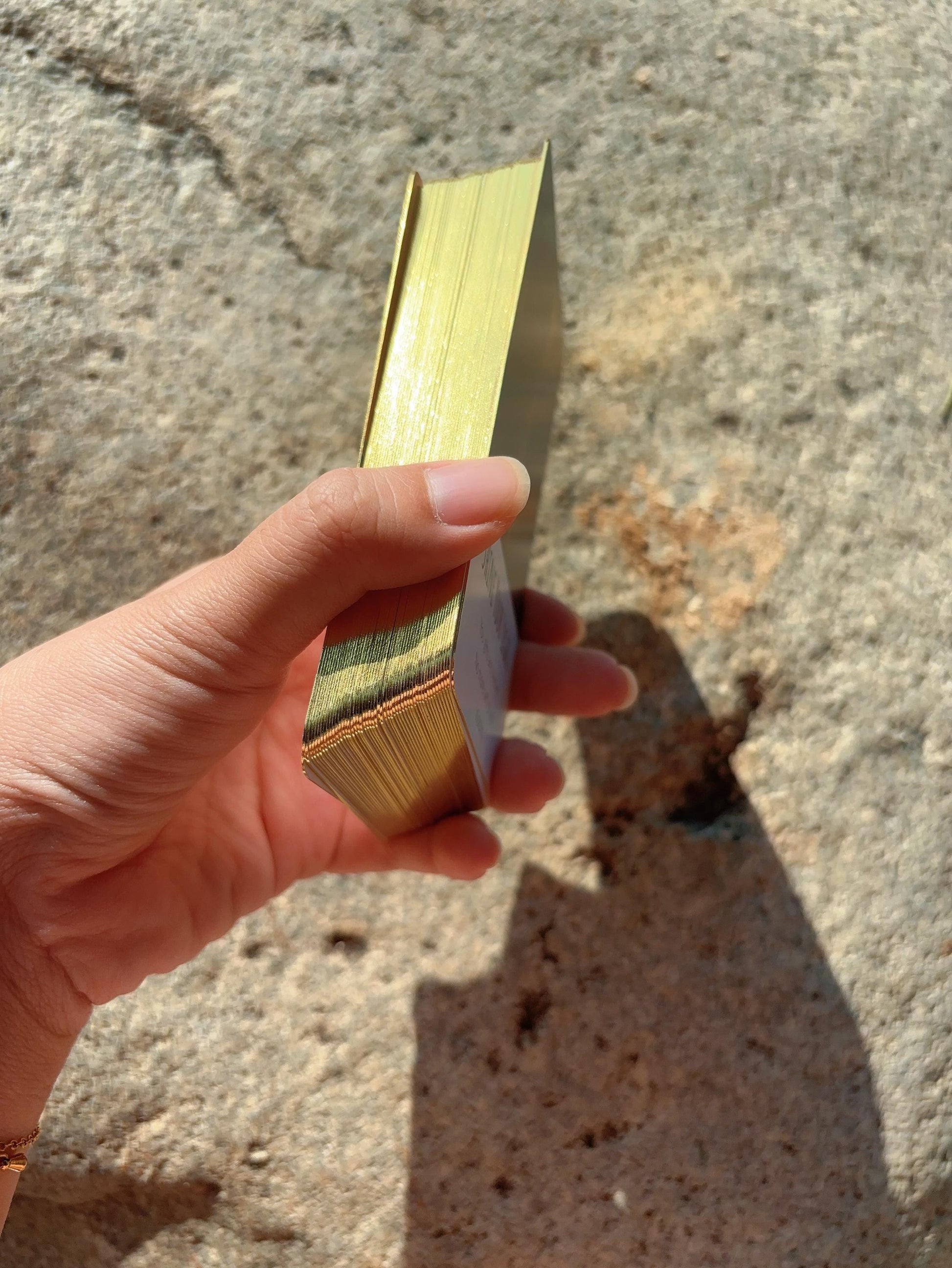 Hand holding Abundance Oracle Deck cards outdoors in sunlight showing gilded gold side of the deck