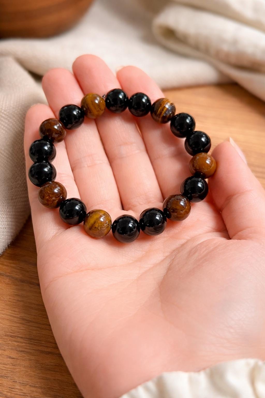 Hand holding a beaded bracelet with black and brown beads on a wooden surface.