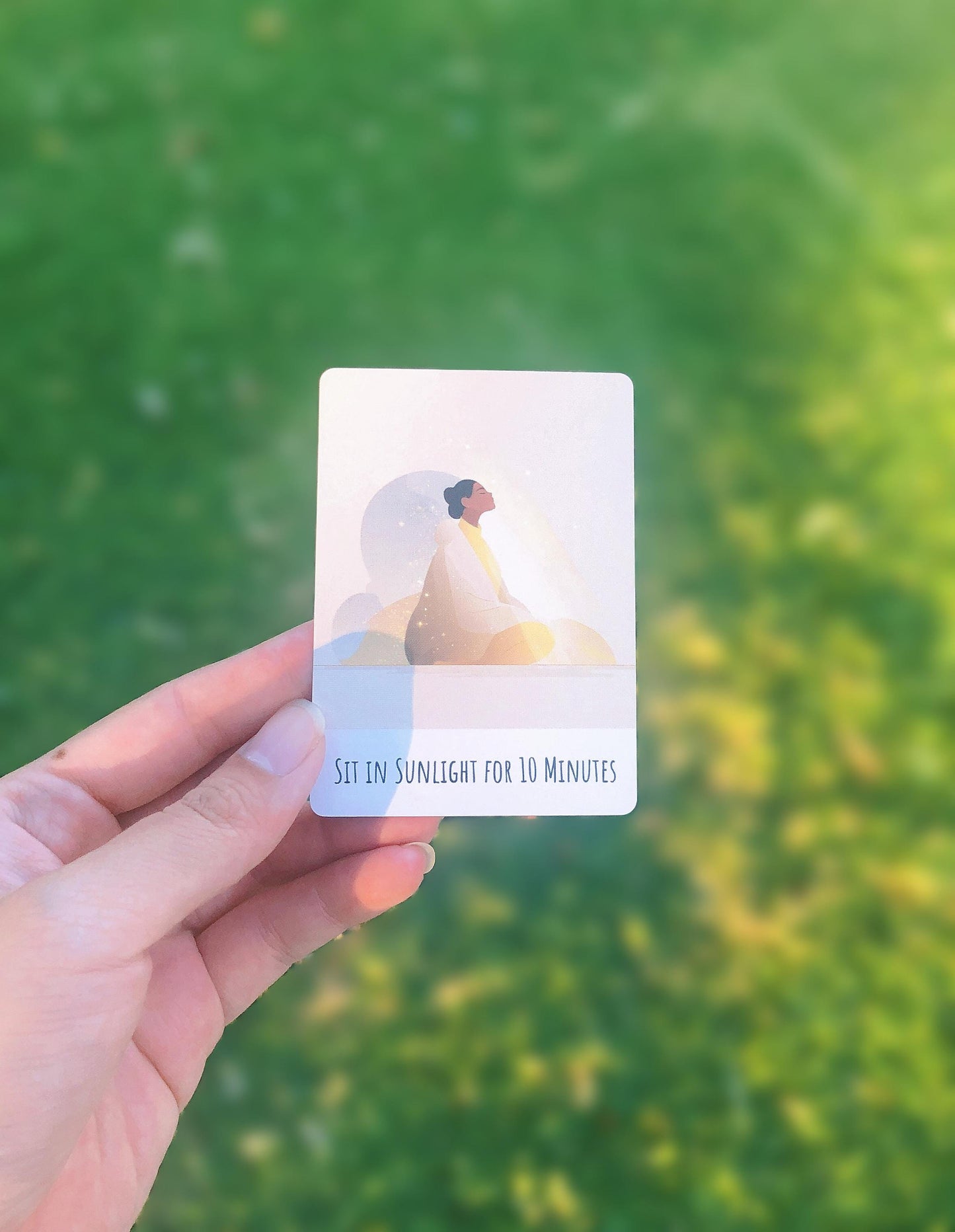 Hand holding a card from the Pocket Ritual Oracle Deck with a sun protection graphic against a green outdoor background