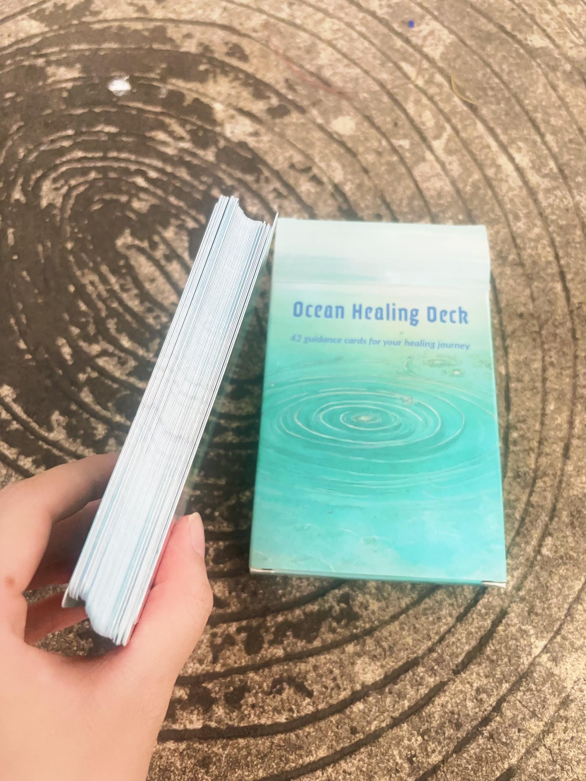 Hand holding a deck of cards titled 'Ocean Healing Deck' on a textured surface.
