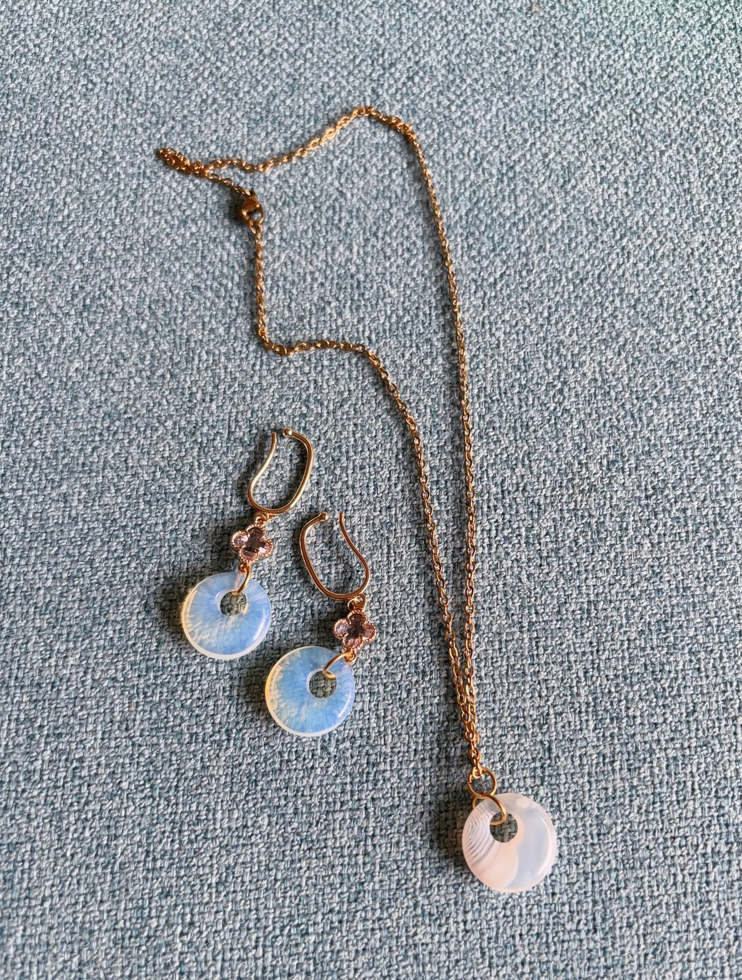 Matching opalite earrings and circular striped agate pendant on a textured gray surface