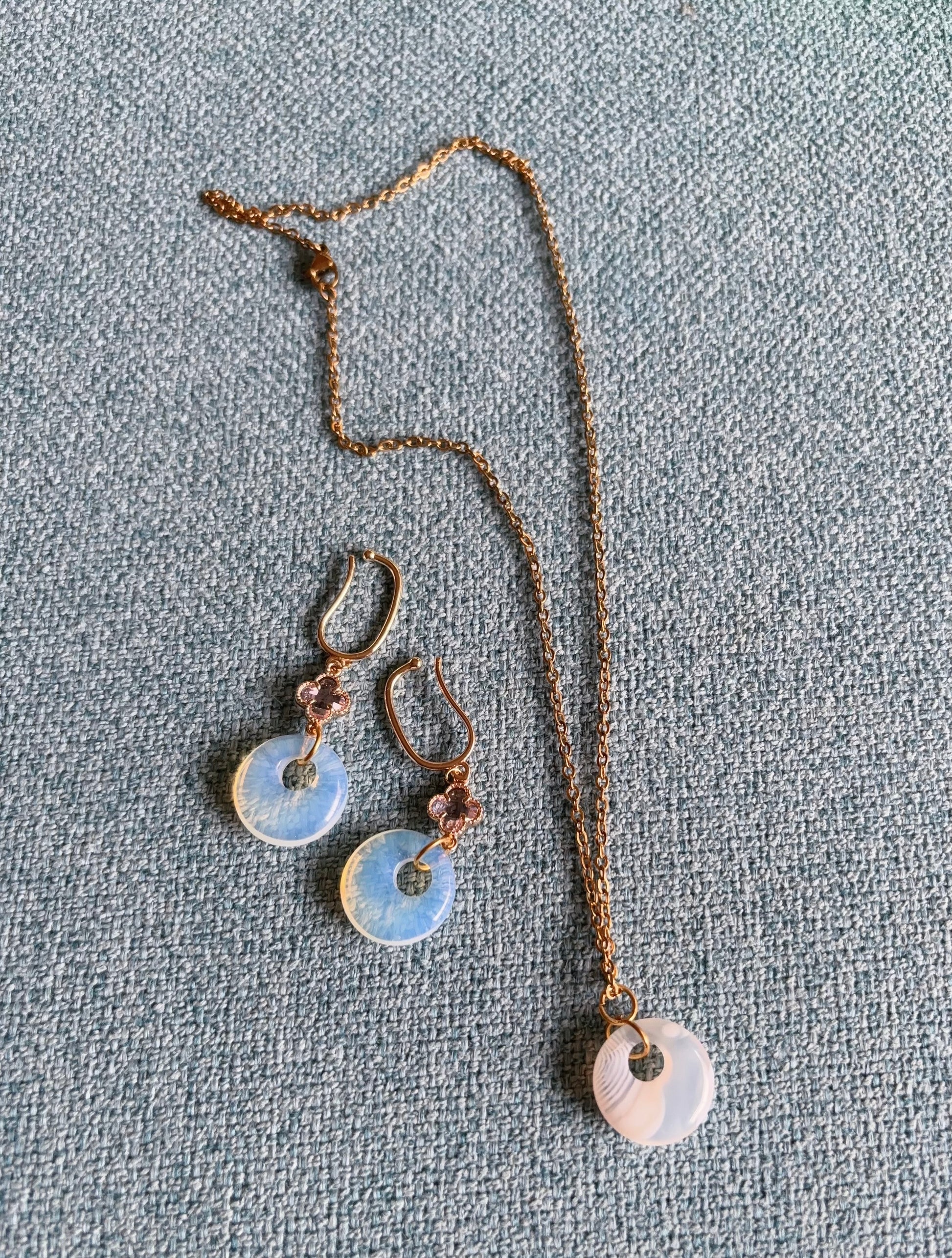 Matching opalite earrings and circular striped agate pendant on a textured gray surface