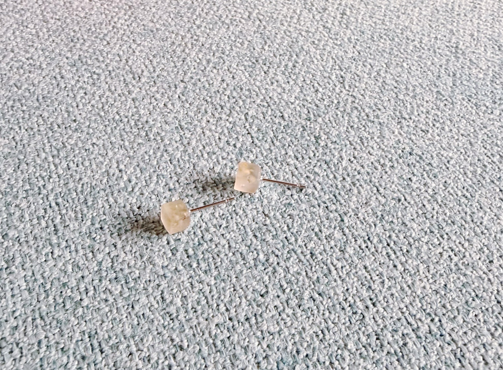 Minimal peridot stud earrings on neutral fabric background