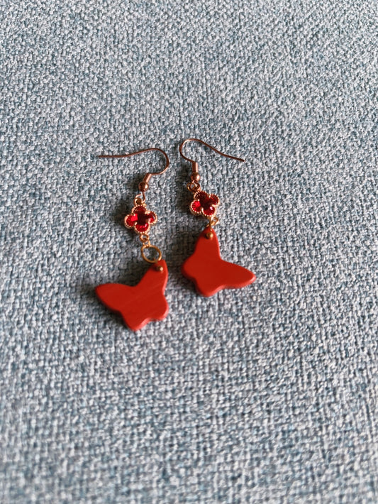 Red jasper butterfly dangle earrings with gold clover charm on textured background
