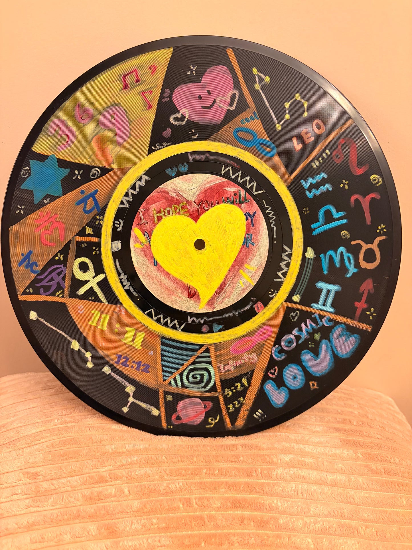 Decorative vinyl record with colorful zodiac symbols on a wooden surface. Intuitive painted vinyl record featuring zodiac signs, heart center, and abstract symbols